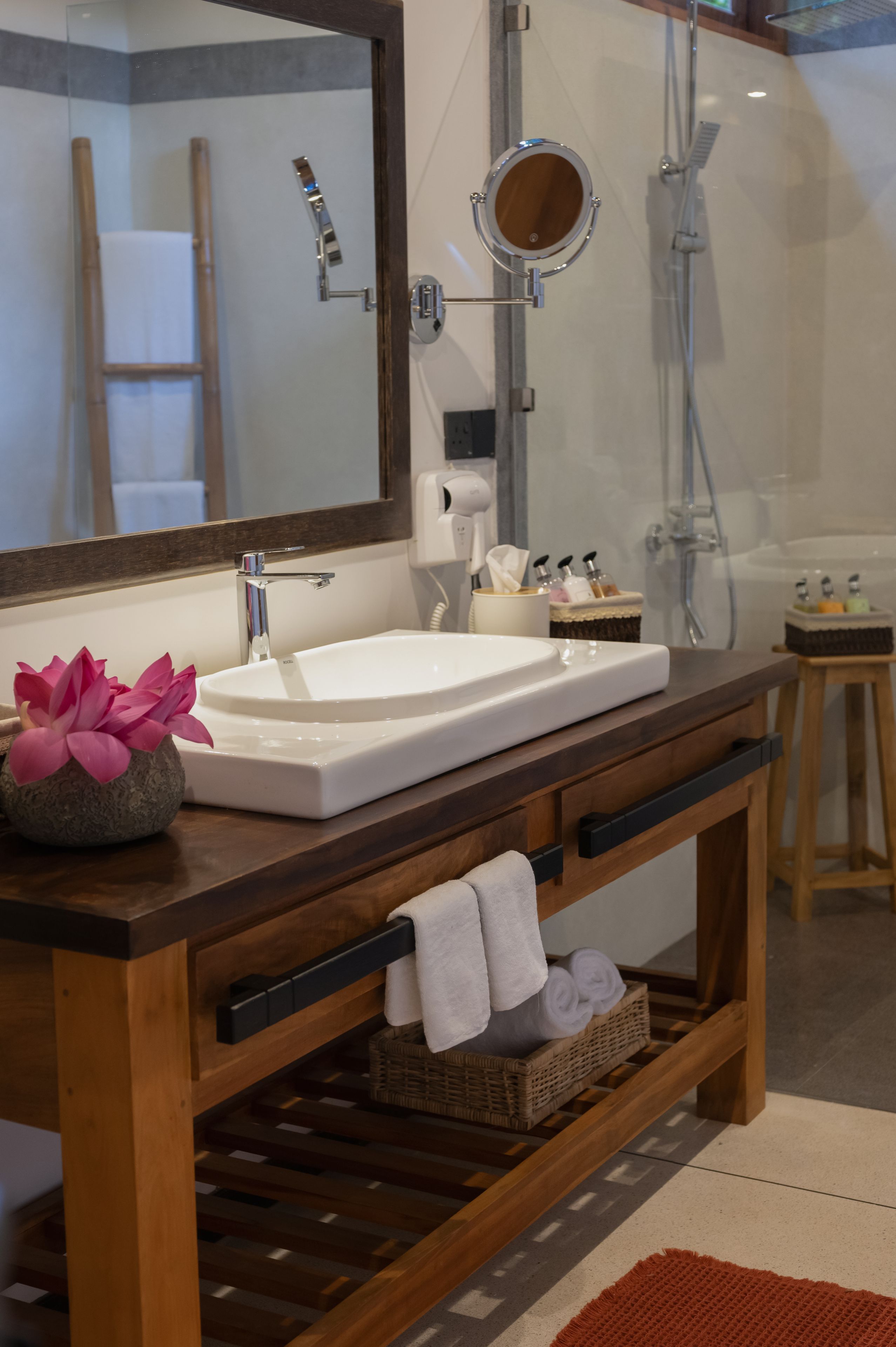 A bathroom with a wooden vanity, a white sink, a mirror, a towel rack, and a shower area.