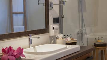 A bathroom with a wooden vanity, a white sink, a mirror, a towel rack, and a shower area.