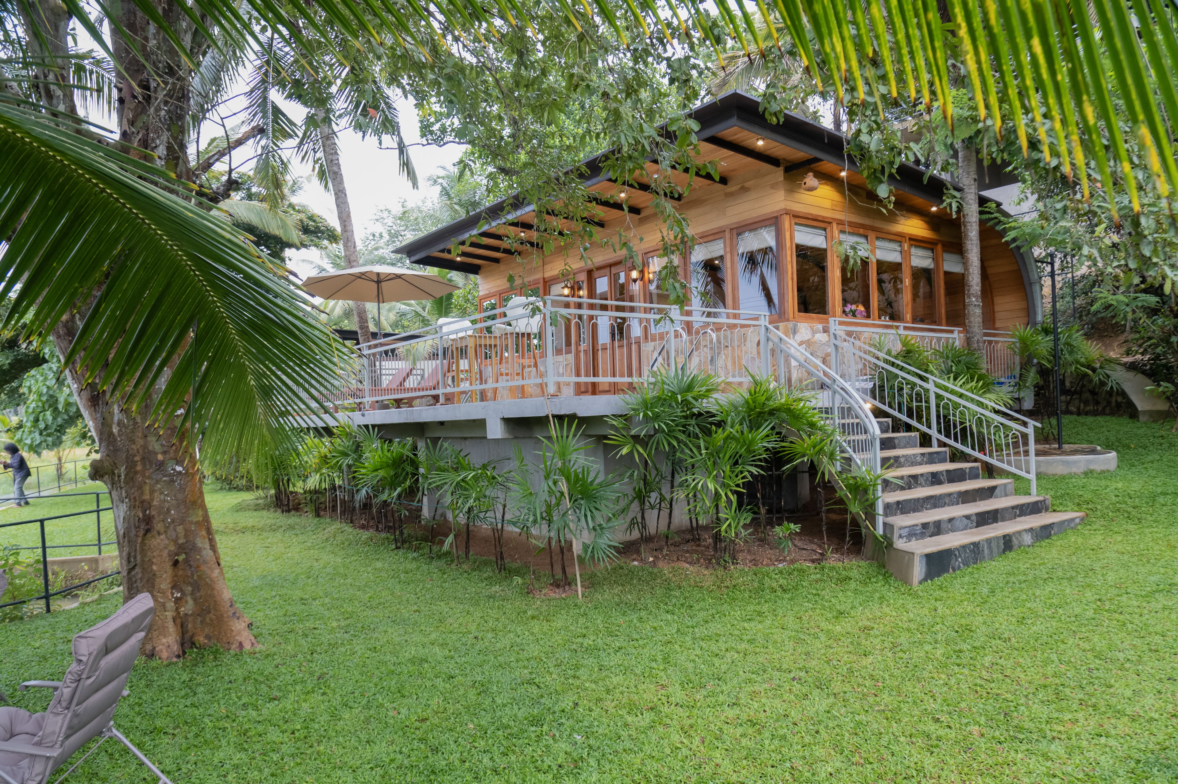 A wooden structure with a balcony, surrounded by lush greenery and a well-maintained lawn.