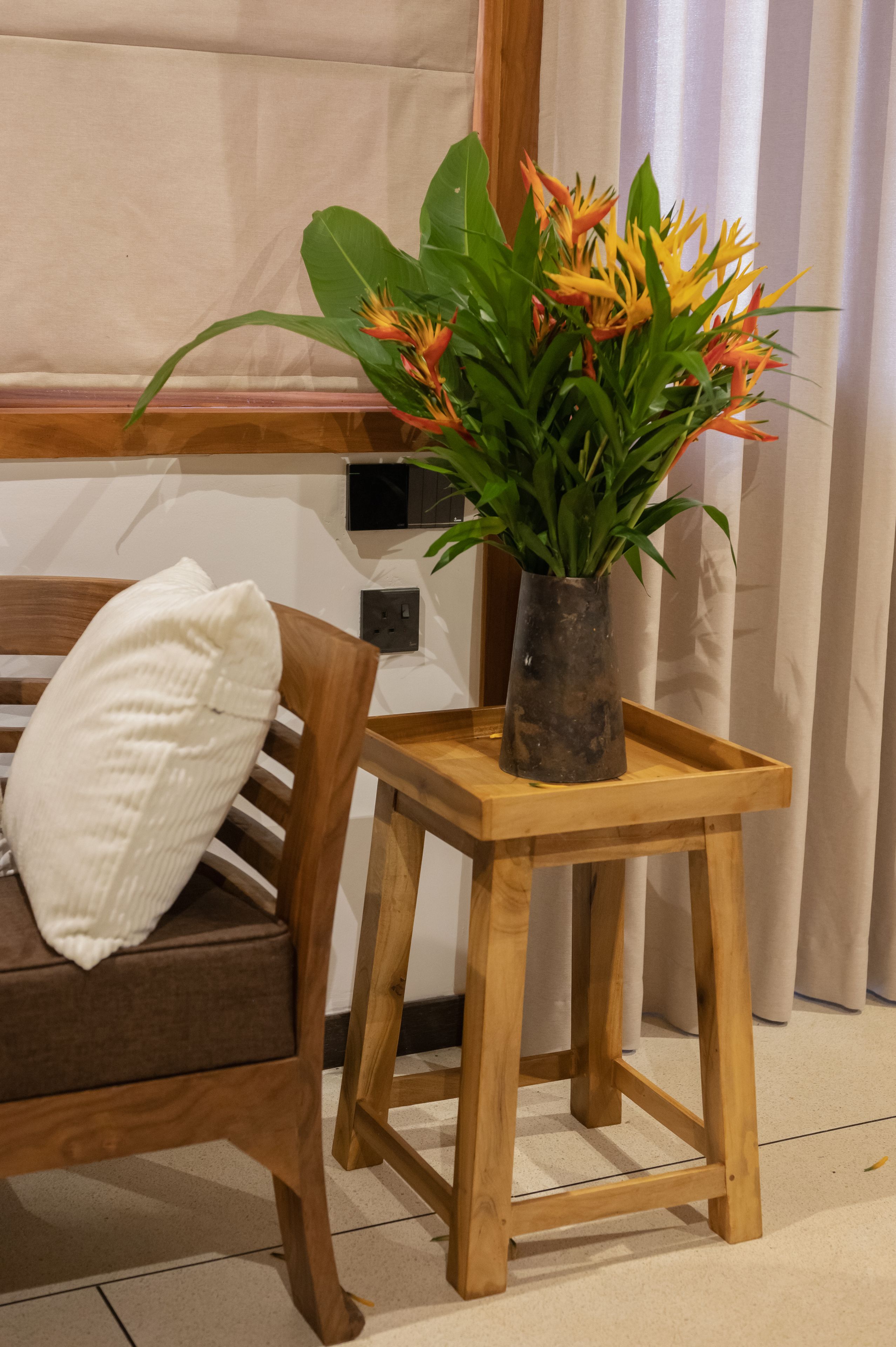 Una silla de madera con un almohadón blanco, una pequeña mesa de madera con un florero y un enchufe en la pared.