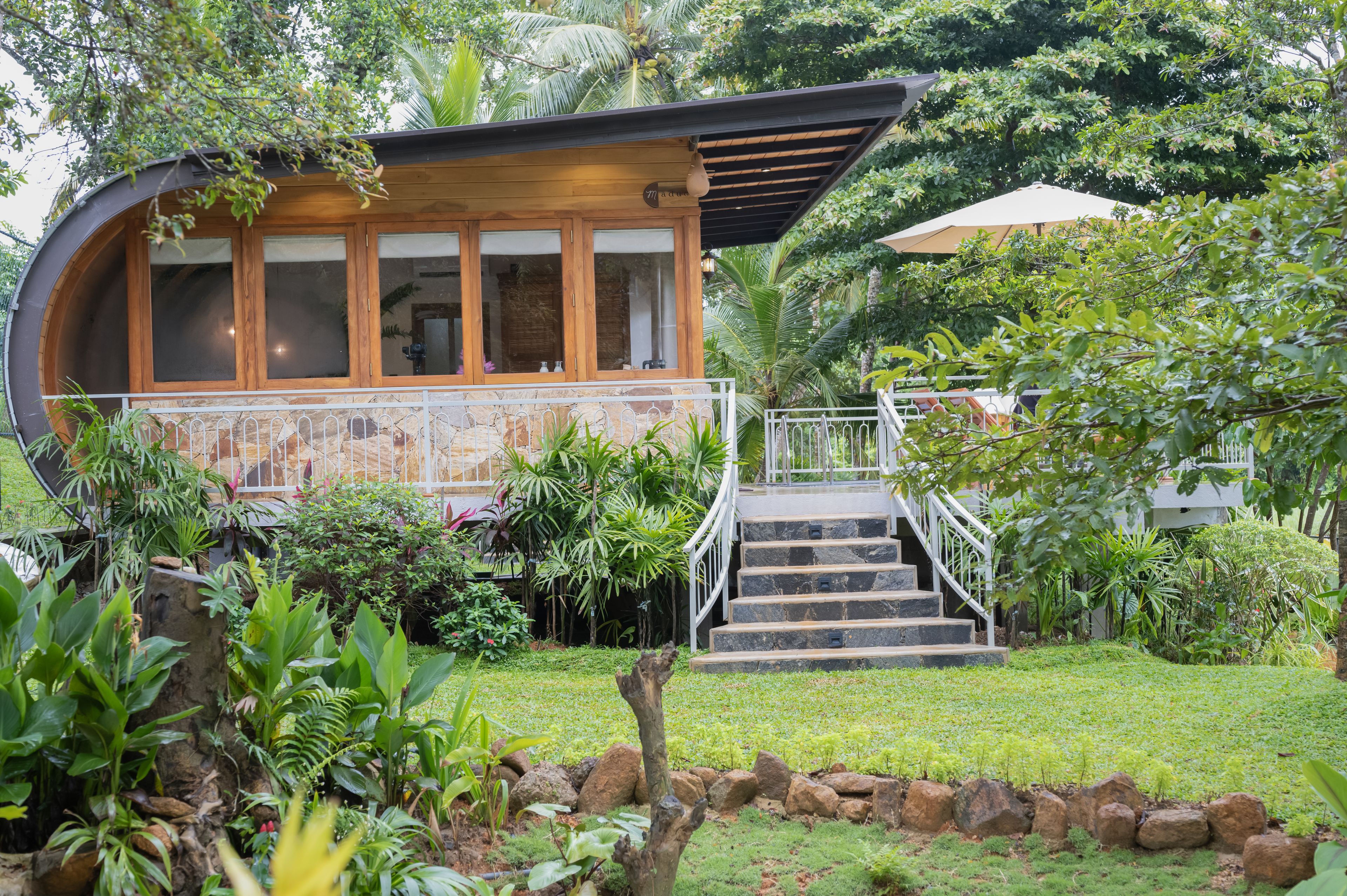 A modern house with a curved wooden facade, a stone lower section, and a staircase leading to a wooden deck.
