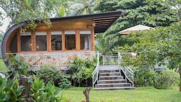 A modern house with a curved wooden facade, a stone lower section, and a staircase leading to a wooden deck.
