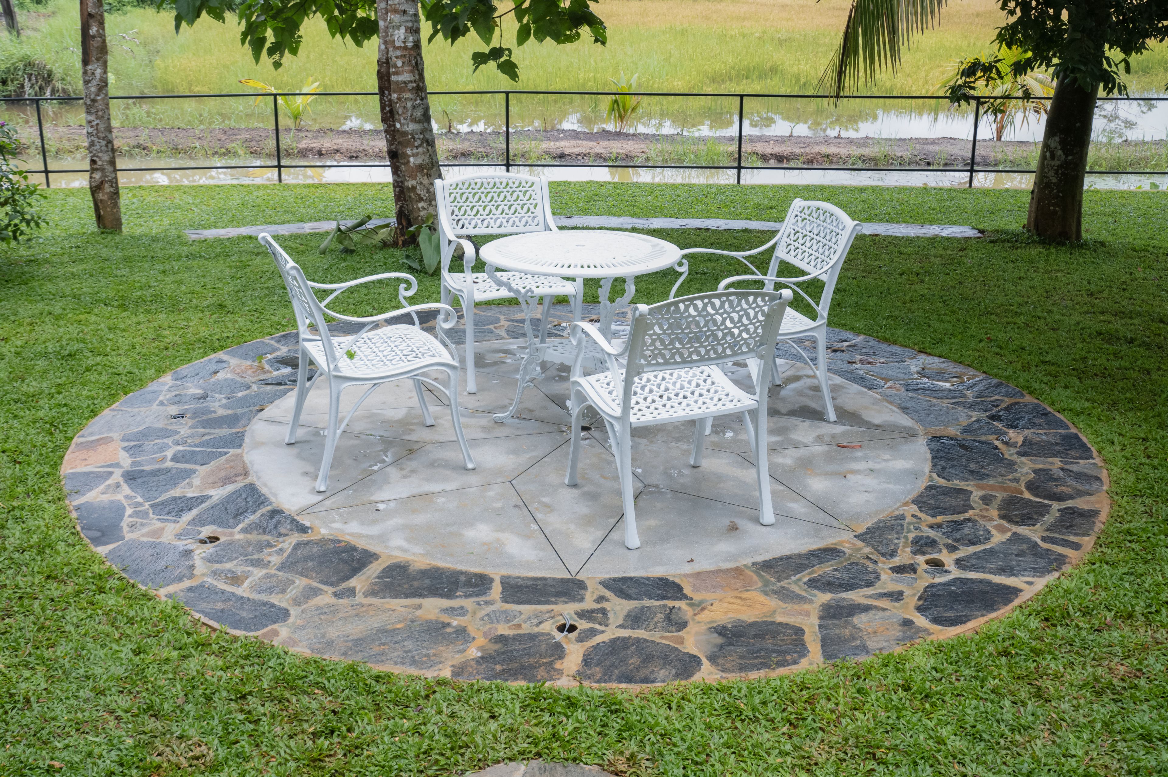 Uma área de estar ao ar livre circular com piso de pedra e cadeiras e mesa de metal branco.