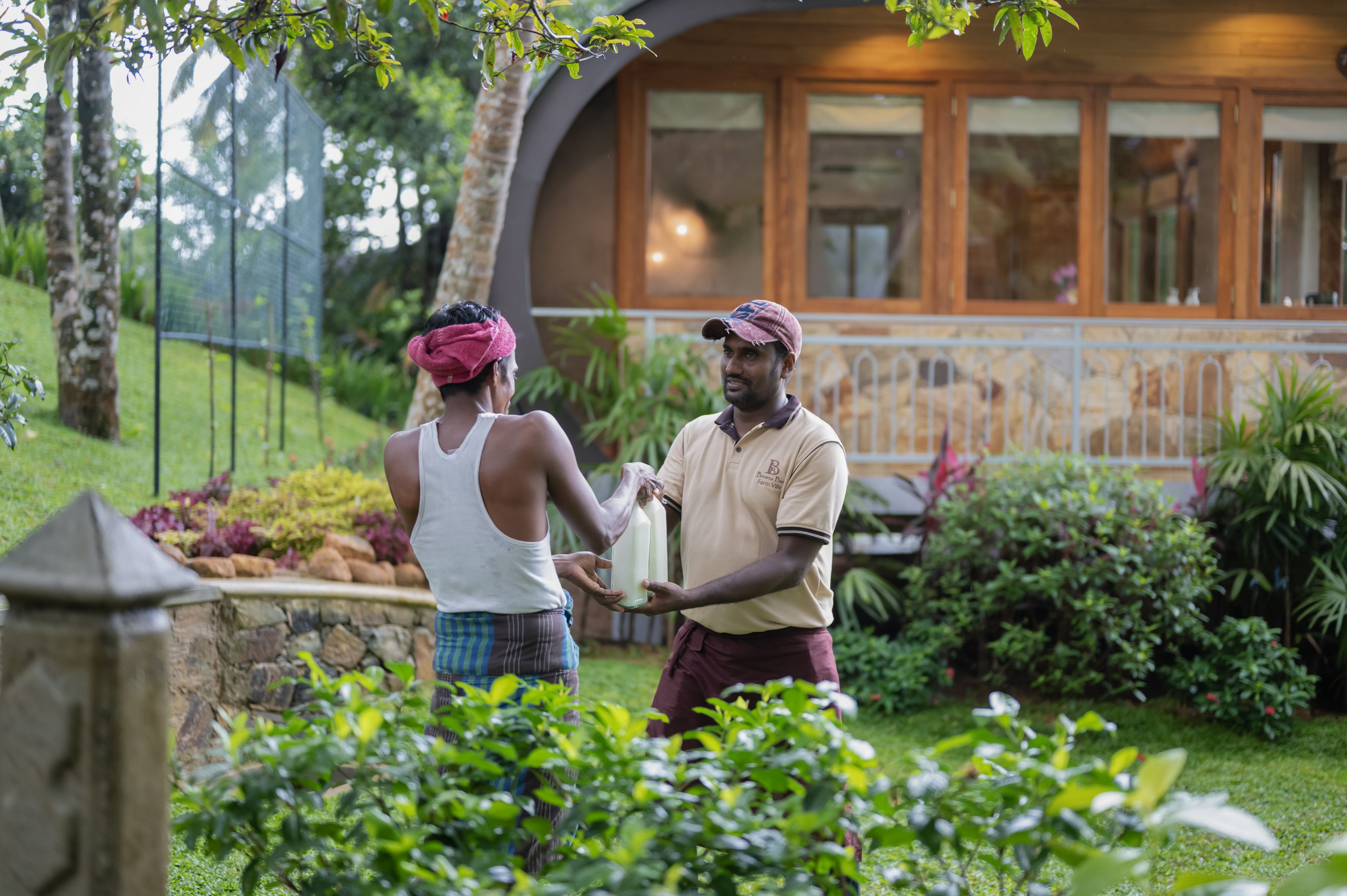 Two individuals in a garden with a house in the background.