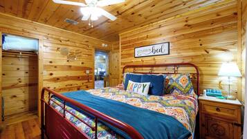 A wooden cabin bedroom with a bed, a nightstand, a ceiling fan, and a sign that says 'Let's stay in bed'.