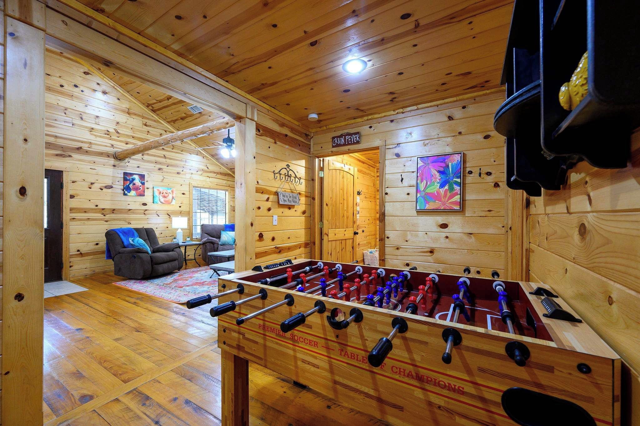A wooden-floored room with a foosball table, a sofa, and a sign reading 'CABIN FEVER'.