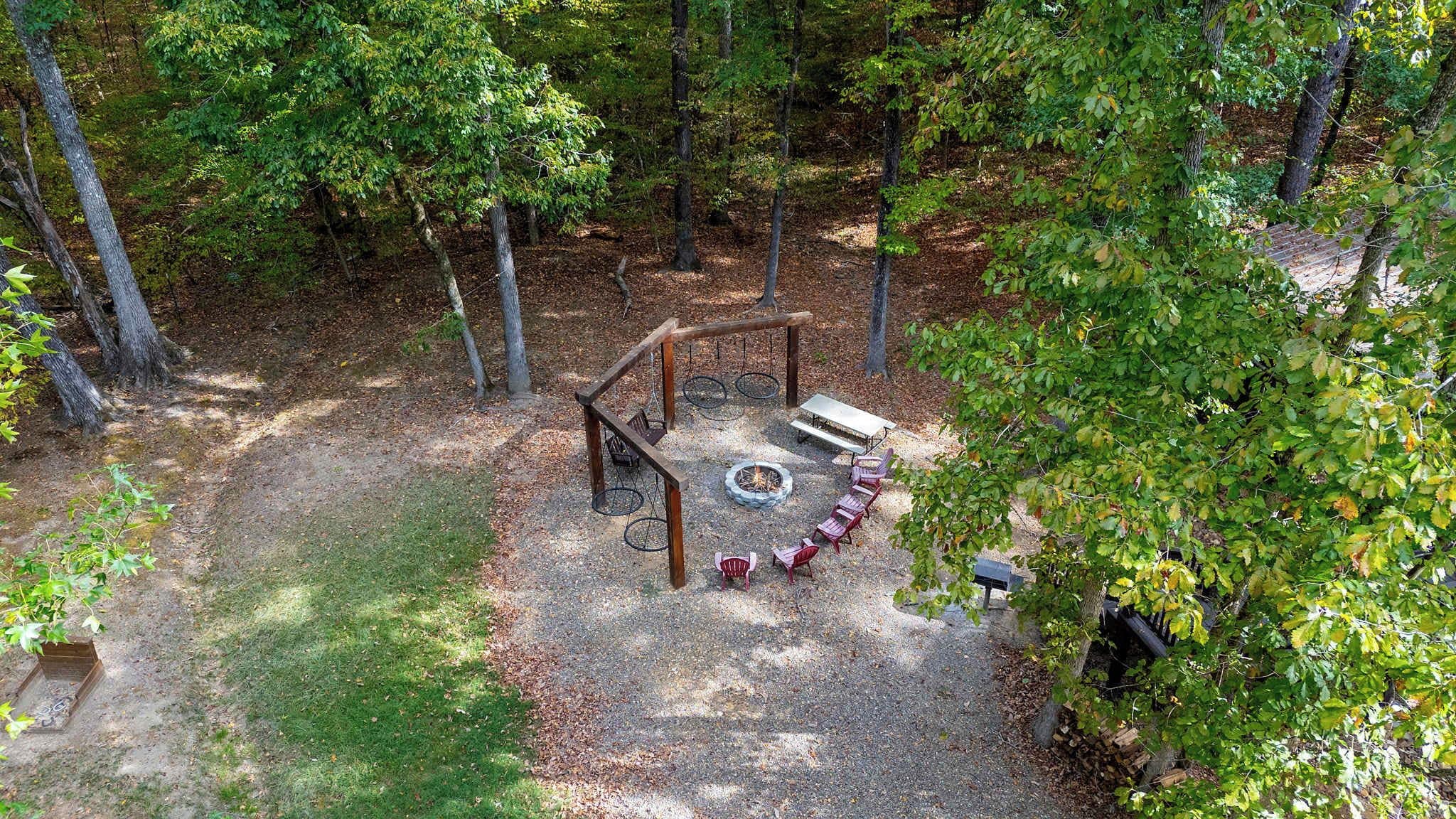 A forested outdoor area with a swing set, fire pit, and seating.