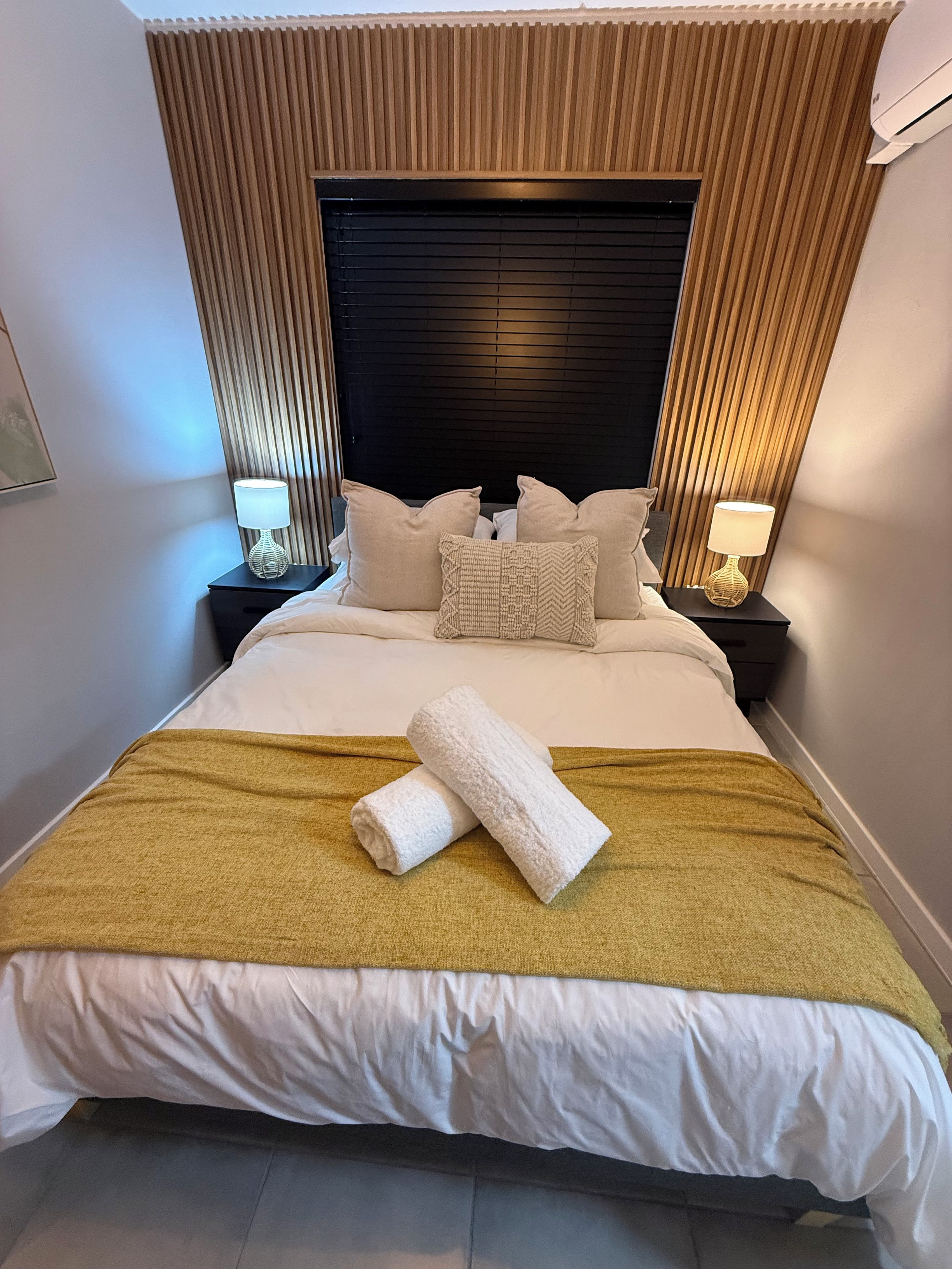 Ein Hotelzimmer mit einem großen Bett, zwei Nachttischen, einem Kopfteil und einem Fenster mit Jalousien.