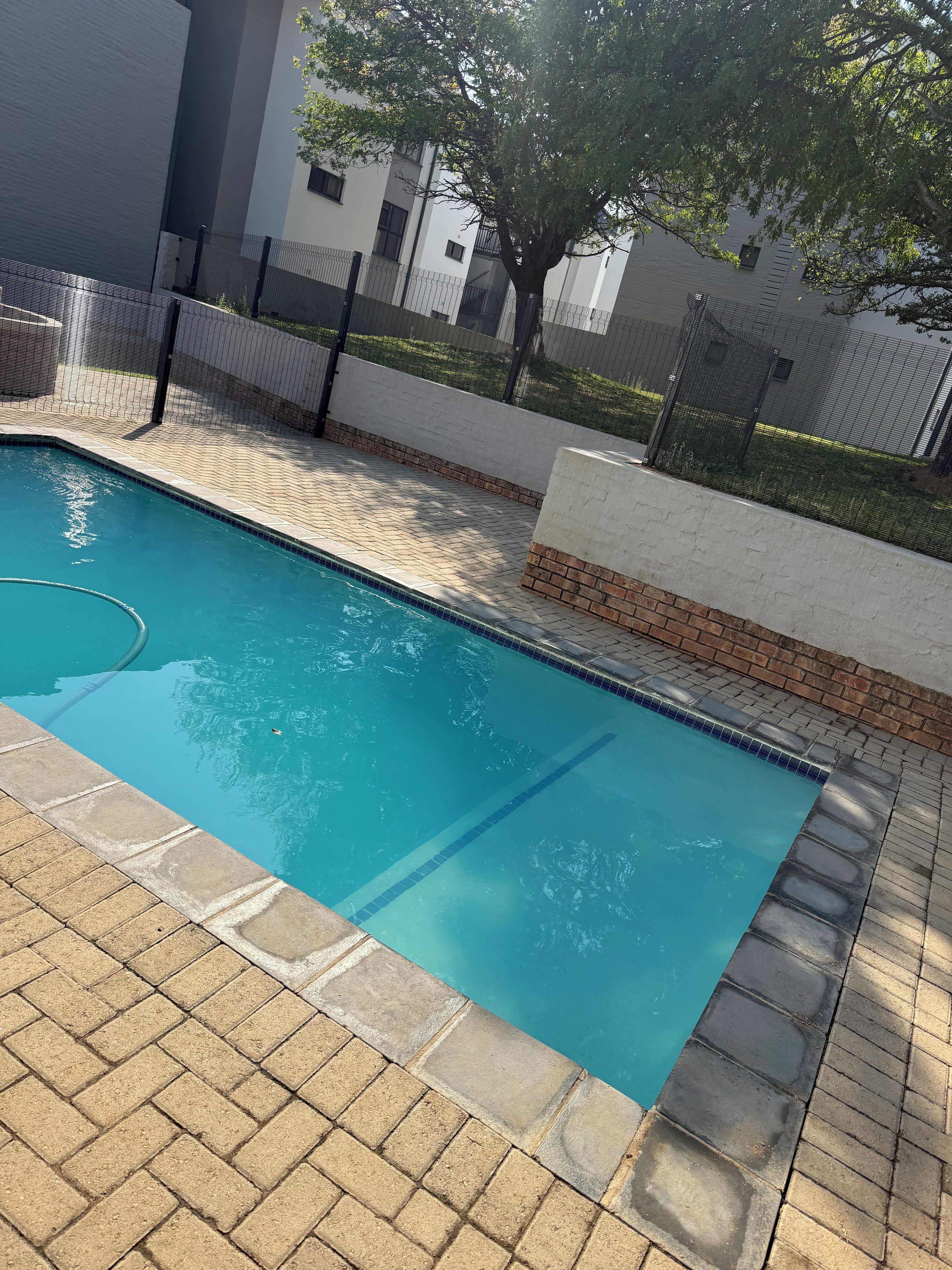 Une piscine dont le bord est revêtu de carreaux, entourée d’une terrasse en briques et d’une clôture.