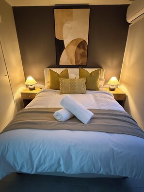 A neatly made bed with a rolled towel, two nightstands with lamps, and a large abstract painting above the bed.