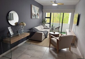 A modern living room with a sofa, armchair, glass coffee table, and a dining area with a table and chairs.