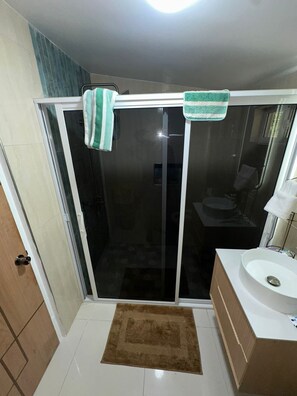 A bathroom with a glass shower enclosure, a white sink, and a brown rug. - Spacious 1BR | Ocean Views & Mountain Escape (St. Ann Parish)