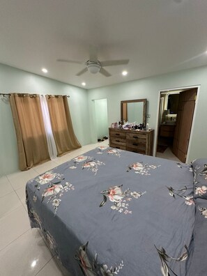 A bedroom with a bed, a dresser, a mirror, and a ceiling fan. - Spacious 1BR | Ocean Views & Mountain Escape (St. Ann Parish)