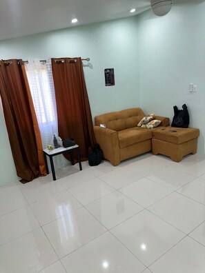 A room with a brown sofa, a small table, and a black bag. - Spacious 1BR | Ocean Views & Mountain Escape (St. Ann Parish)