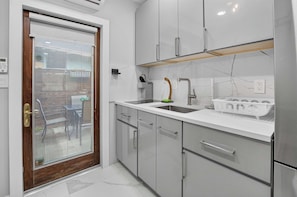 A modern kitchen with a white countertop, stainless steel appliances, and a wooden door with a glass panel. - Marina Row 2 Coastal Studio (Delray Beach)