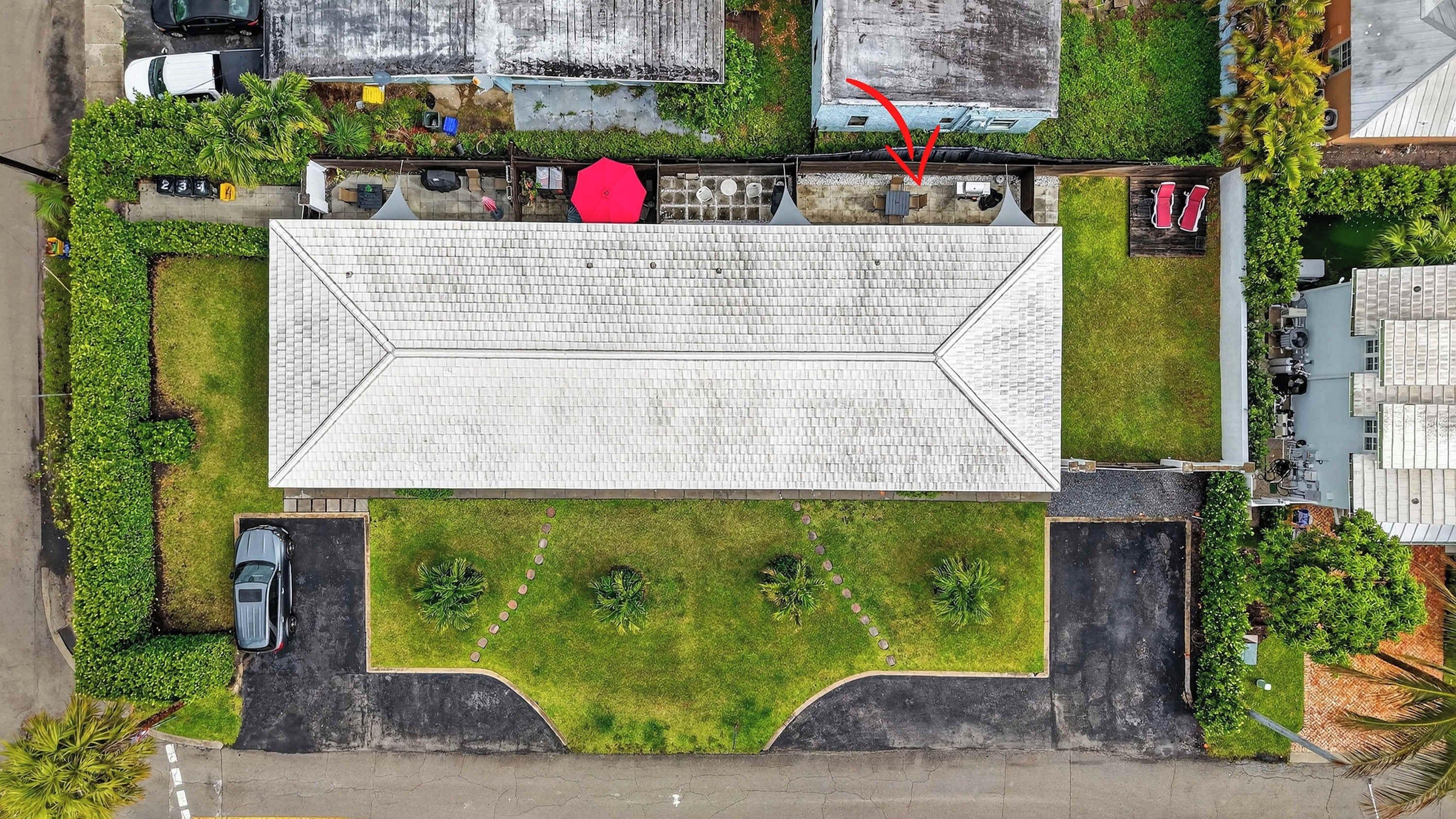 An aerial view of a building with a flat roof, surrounded by greenery and parking spaces.