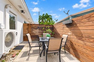 Un patio exterior con una mesa y sillas, una valla de madera y un equipo de aire acondicionado.