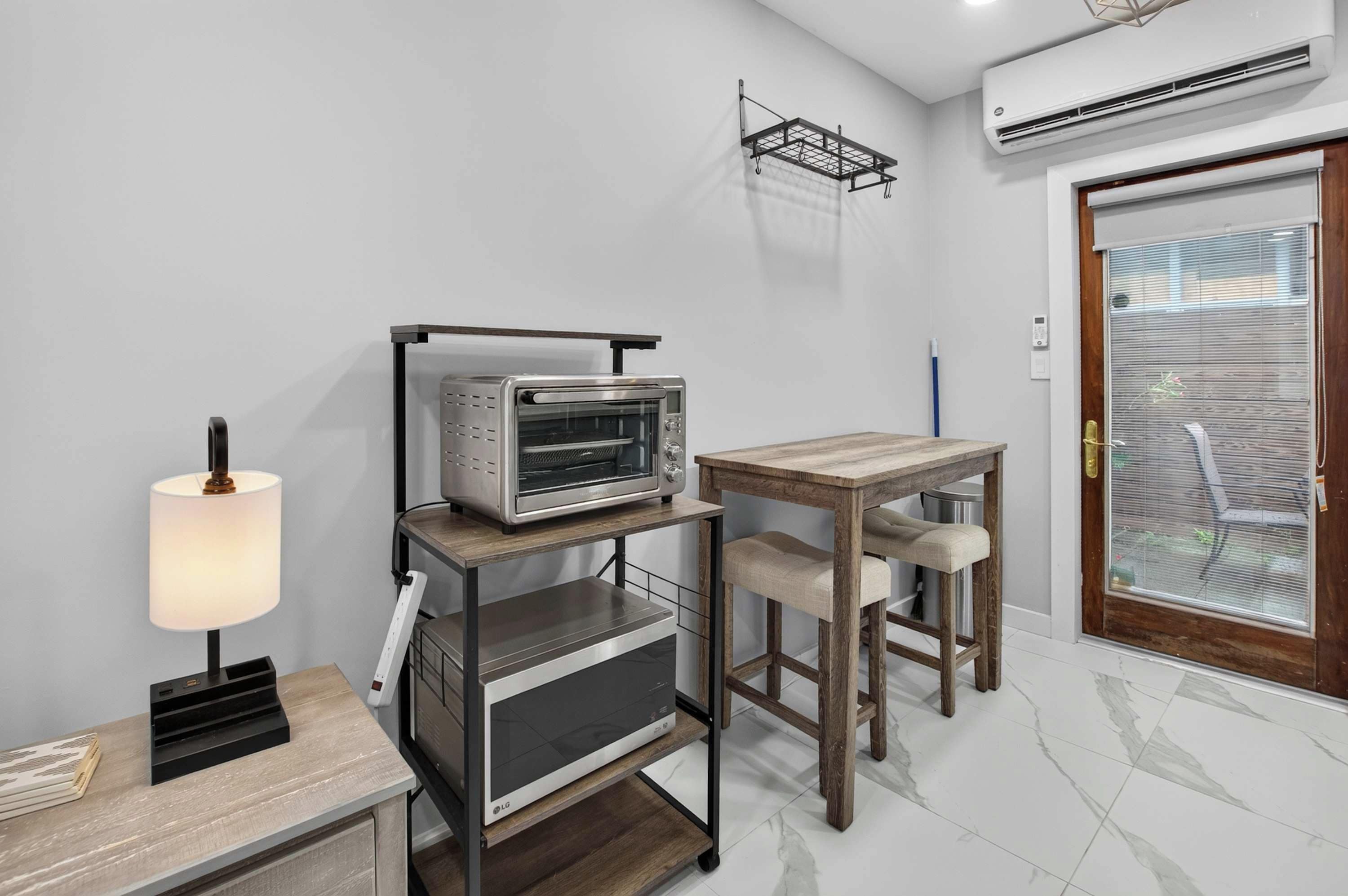 A kitchenette with a built-in oven, a table with chairs, a lamp, and an air conditioning unit.