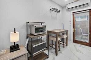 A kitchenette with a built-in oven, a table with chairs, a lamp, and an air conditioning unit. - Marina Row 2 Coastal Studio (Delray Beach)