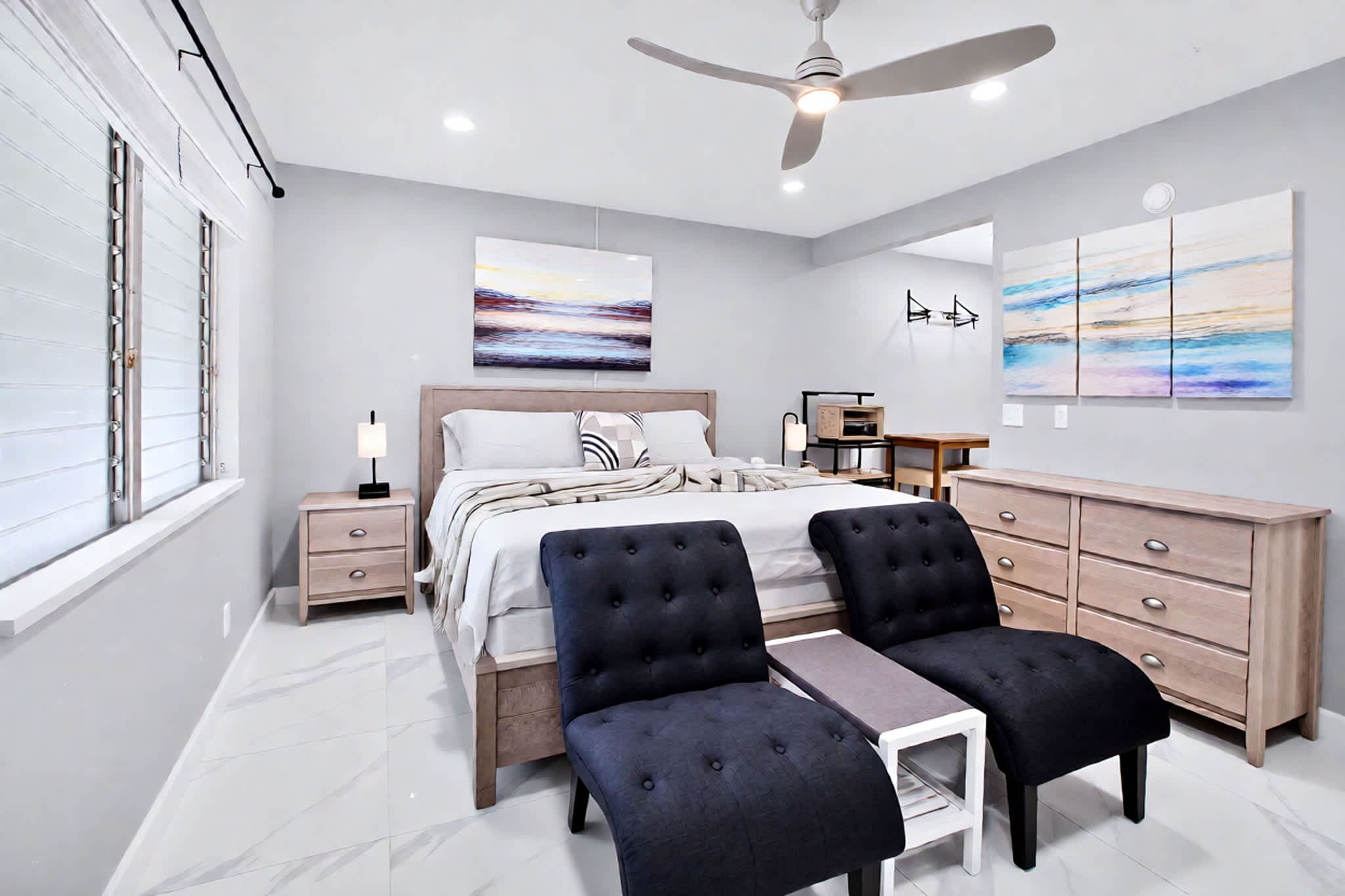 A modern bedroom with a bed, two armchairs, a desk, and a dresser.