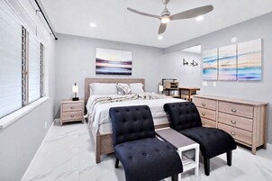 Un dormitorio moderno con cama, dos sillones, un escritorio y un aparador.