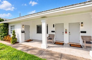 Un espacio al aire libre cubierto con un edificio blanco, una puerta, un banco y un pequeño jardín.
