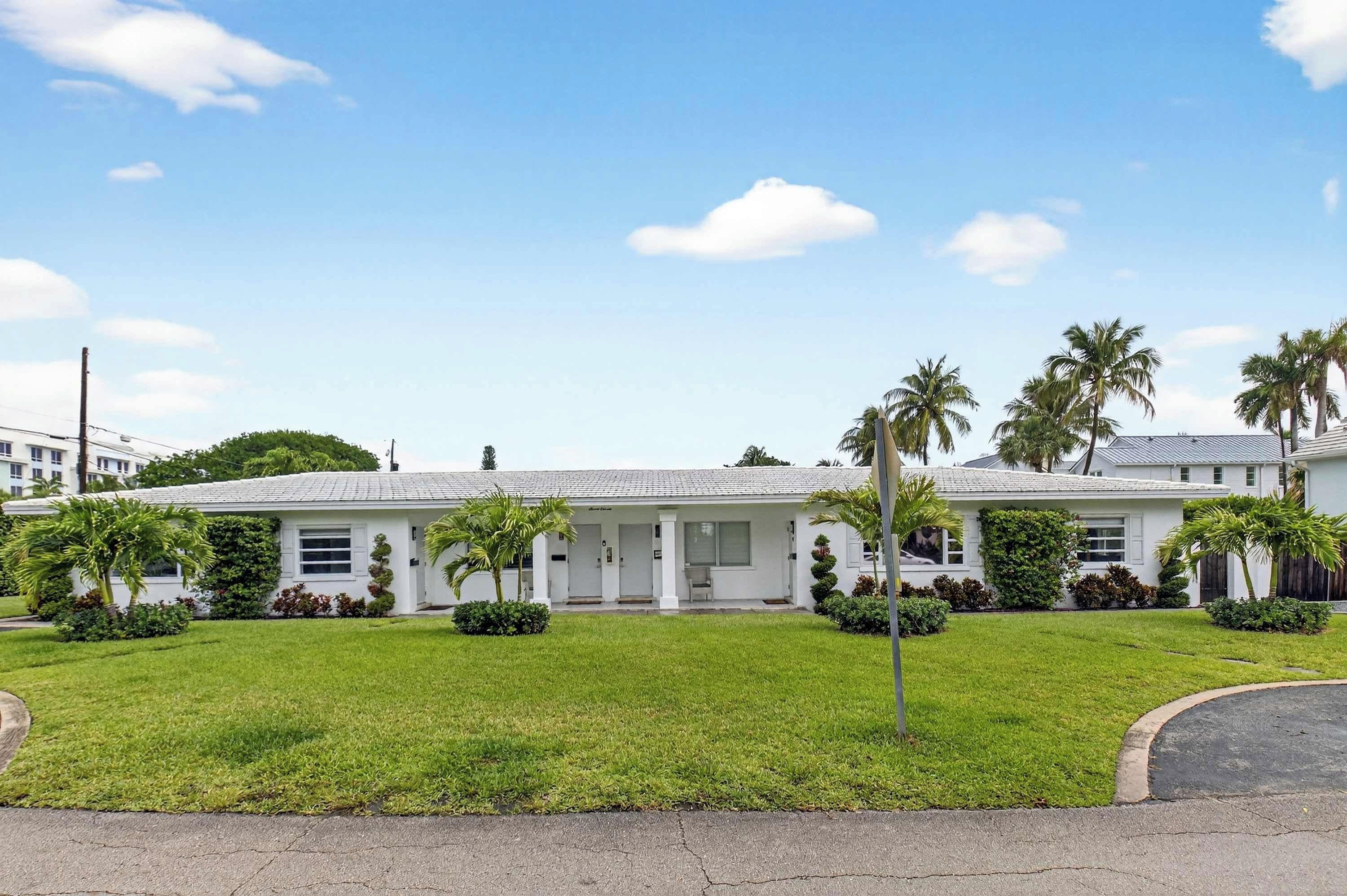 A white building with a flat roof, surrounded by well-maintained grass and palm trees.