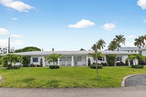 Un edificio blanco con techo plano, rodeado de césped cuidado y palmeras.