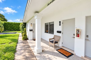 A clean, modern exterior of a building with a covered porch, a fire extinguisher mounted on the wall, and a door with a mailbox. - Marina Row 2 Coastal Studio (Delray Beach)