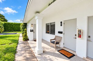 A clean, modern exterior of a building with a covered porch, a fire extinguisher mounted on the wall, and a door with a mailbox.