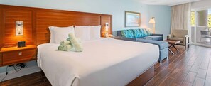 A hotel room with a large bed, a wooden headboard, a nightstand with a phone, a sofa, a chair, and a view of the outdoors. - Margaritaville Vacation Club - St. Thomas USVI Luxury Wyndham Studio Plus Suite (St Thomas)