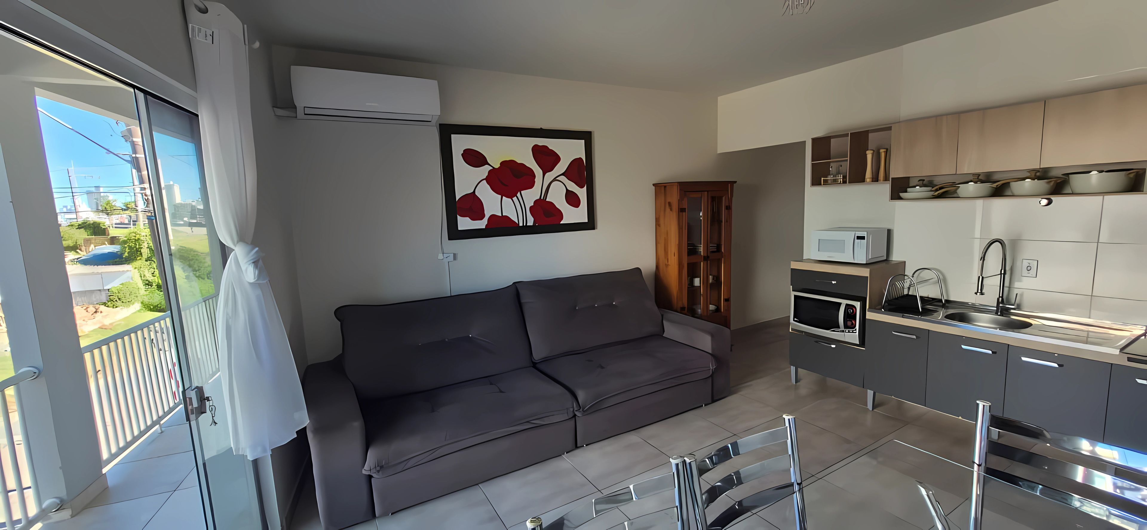 A modern living space with a grey sofa, a kitchen with a built-in microwave, and a dining area with a glass table.