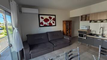 A modern living space with a grey sofa, a kitchen with a built-in microwave, and a dining area with a glass table.