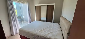 Una habitación con cama, ventana con cortinas y puerta que da a otra habitación.