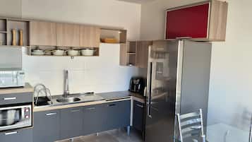 Eine moderne Küche mit grauen Schränken, einem Edelstahl-Kühlschrank, einem eingebauten Backofen und einer Kaffeemaschine.