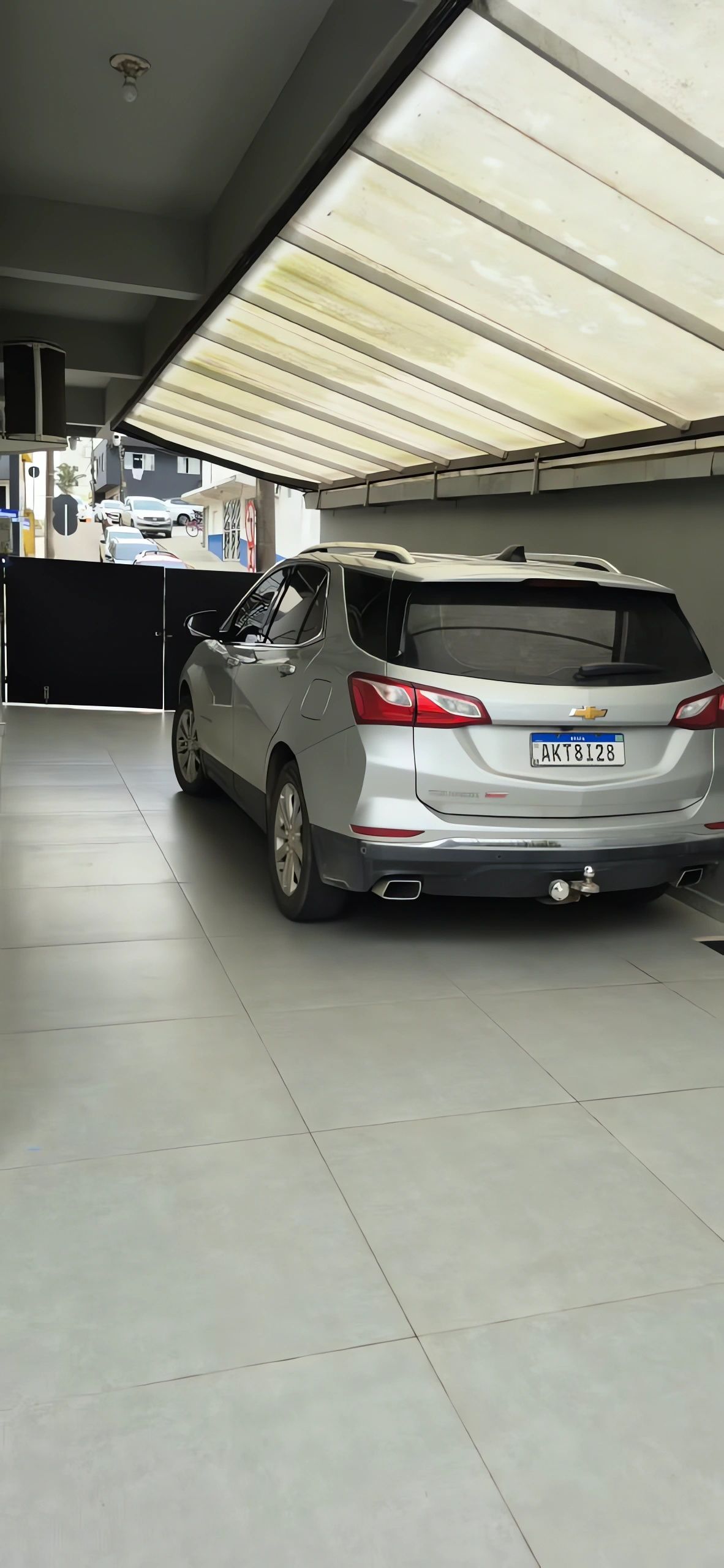 Um SUV Chevrolet prateado estacionado em uma garagem com piso de azulejos e teto com lâmpadas fluorescentes.