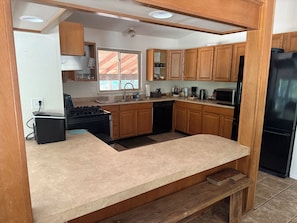A kitchen with wooden cabinets, a black refrigerator, a stove, and a sink. - Riverside Horse Ranch Unplugged (Thornton)