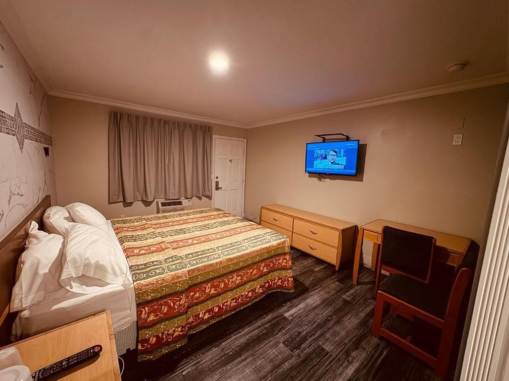 A hotel room with a bed, a TV, a desk, and a chair.