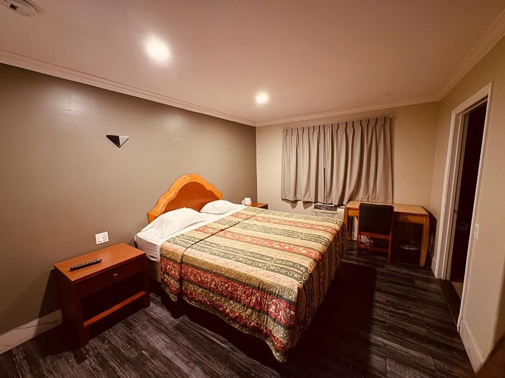 A hotel room with a bed, bedside table, chair, and a desk with a chair.