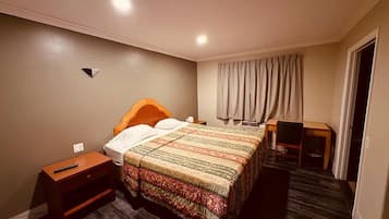 Ein Hotelzimmer mit einem Bett, einem Nachttisch, einem Sessel und einem Schreibtisch mit Stuhl.