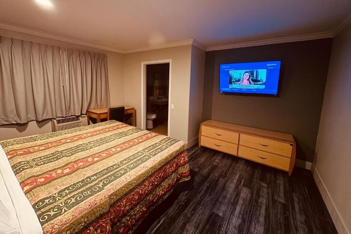 Habitación de hotel con cama, televisor montado en la pared, escritorio y armario.