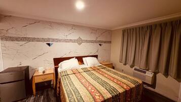 A hotel room with a bed, a nightstand, a heater, and a wardrobe.