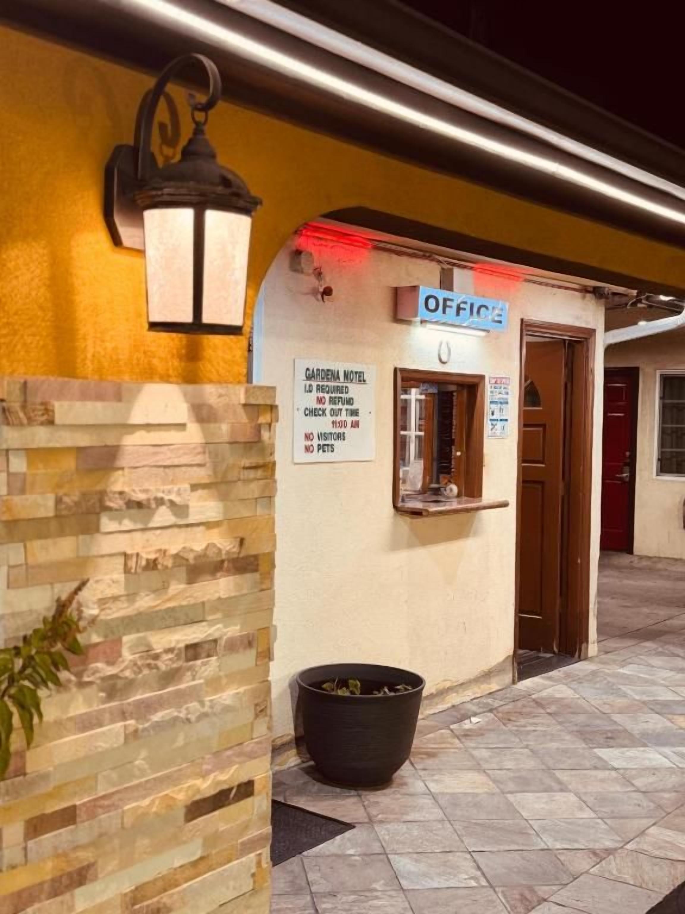 A hotel entrance with a sign indicating 'OFFICE' and a 'GARDENIA HOTEL' sign with a no pets policy.