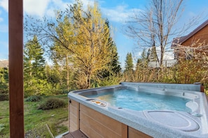Un jacuzzi en una terraza de madera, con un paisaje natural de árboles y un edificio de fondo.