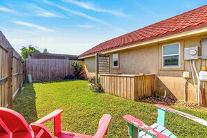 A residential backyard with a wooden fence, a red chair, and a small shed. - Siesta Villa | Private Patio | Dog Friendly (Port Aransas)
