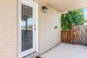 Un patio cubierto con puerta corrediza de vidrio, una lámpara de pared y una valla de madera.