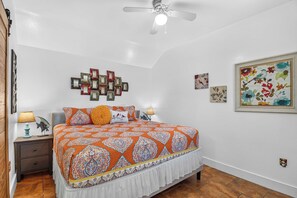 A bedroom with a bed, two bedside lamps, a ceiling fan, and a wall with framed artwork. - Siesta Villa | Private Patio | Dog Friendly (Port Aransas)
