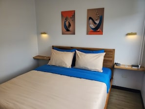 Quarto com cama, duas mesas de cabeceira, um criado-mudo e duas luminárias fixadas na parede.