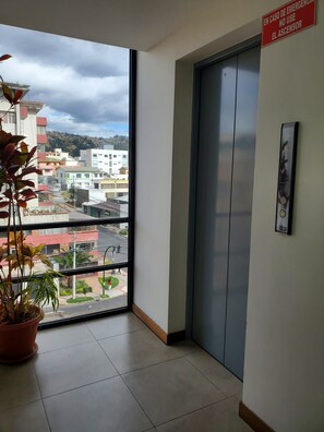 A room with a large window, a potted plant, and an elevator. - QuitoVibes4U ¡Elegante, ubicación privilegiada, acogedor! (Quito)
