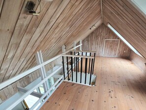 Ein Dachzimmer mit Holzscheiben an der Decke, einer weißen Treppe und einem Holzboden.